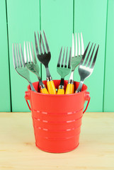 Forks in metal bucket on color wooden background