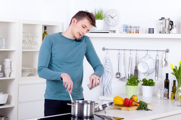 young man cooking a meal and talking on the phone in the kitchen