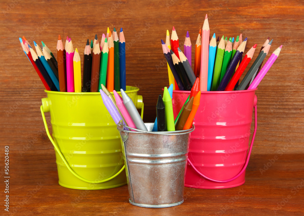Colorful pencils in three pails on wooden background