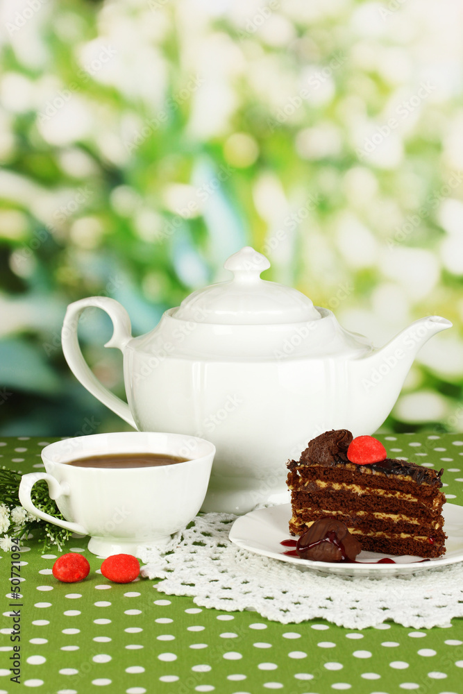 Teapot, cup of tea and delicious cake on natural background