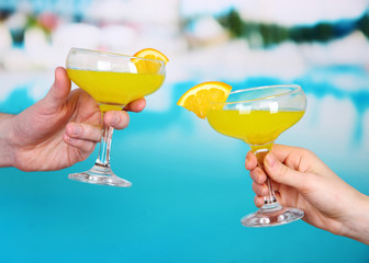 Cocktails in men's and women's hands on pool background