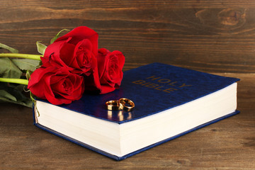 Wall Mural - Wedding rings on bible with roses on wooden background