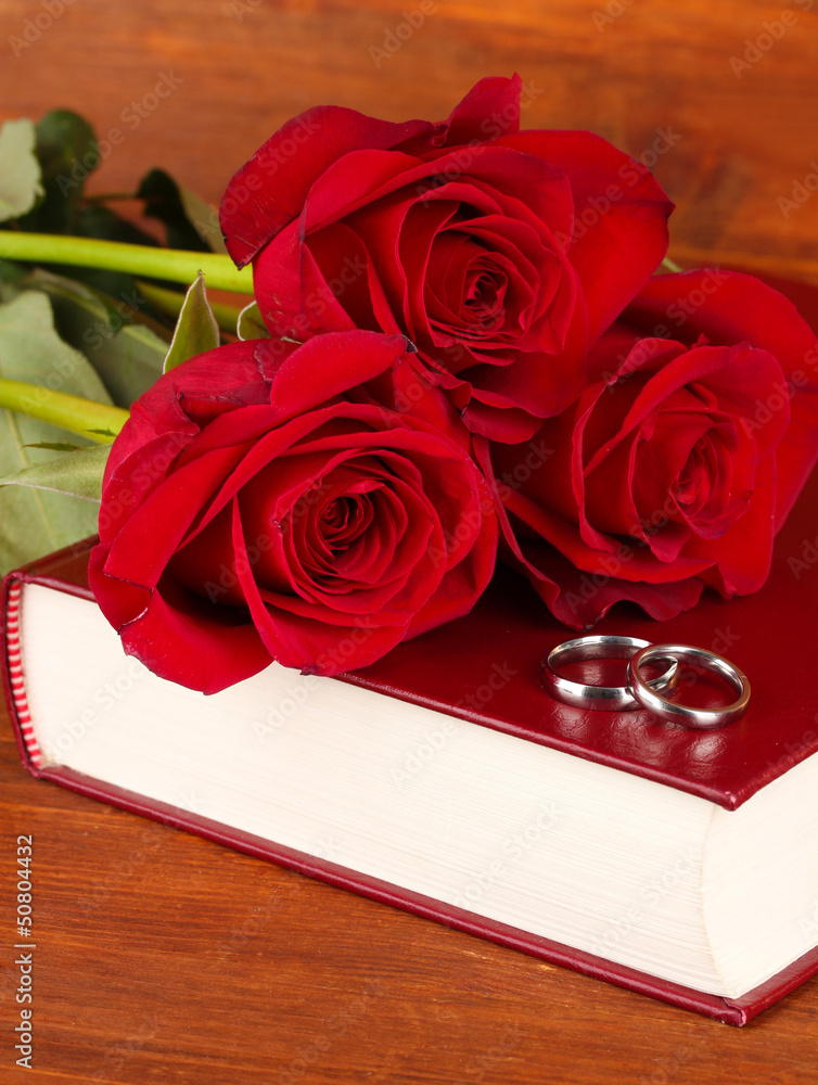 Wedding rings on bible with roses on wooden background
