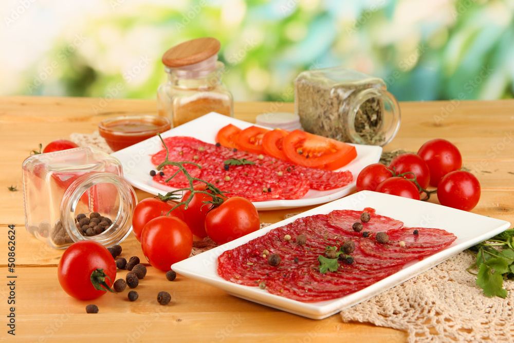 Tasty salami on plates on wooden table on natural background
