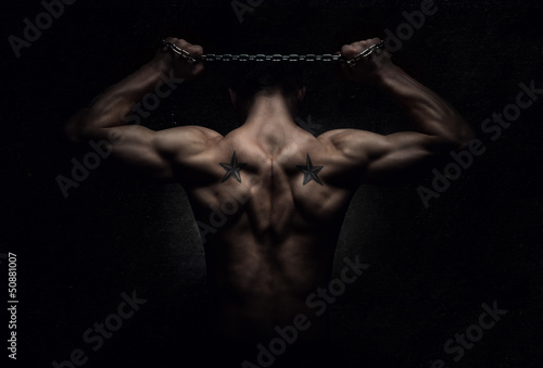 Fotomural Muscular sports man stretching out over dark background