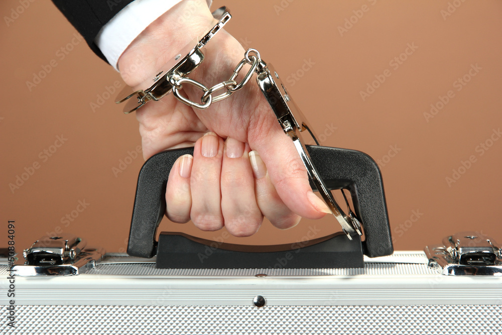 Hand with handcuff and suitcase, on color background