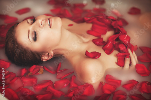 Fototapeta na wymiar Woman in bath at spa in milk with roses petals