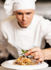 Chef decorating pasta salad with herbal leaves