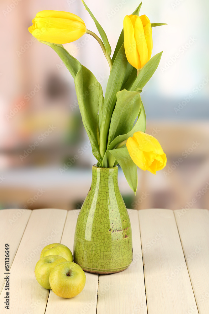 Yellow tulips in vase on wooden table on room background