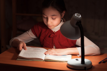 girl at desk reading a book by light of the lamp