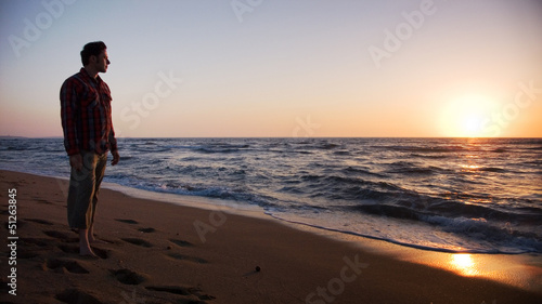 Cuadros en Lienzo Man standing on the beach and looking into sunset