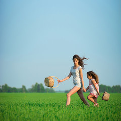 Young happy girls running witch baskets at green wheat field