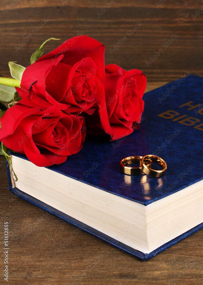 Wedding rings on bible with roses on wooden background