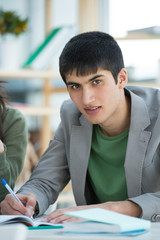 Wall Mural - handsome male student looking at camera while making notes sitti