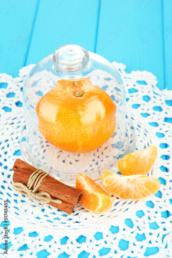 Tangerine on saucer under glass cover on blue background