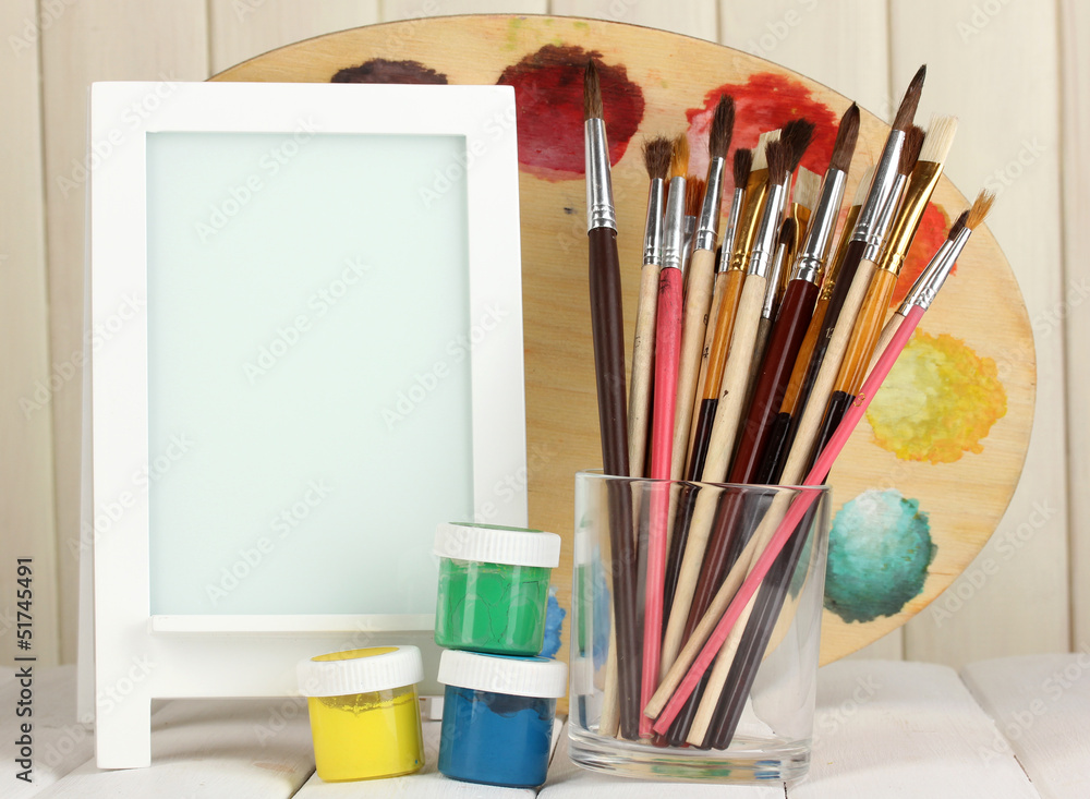 Photo frame as easel with artist's tools on wooden background