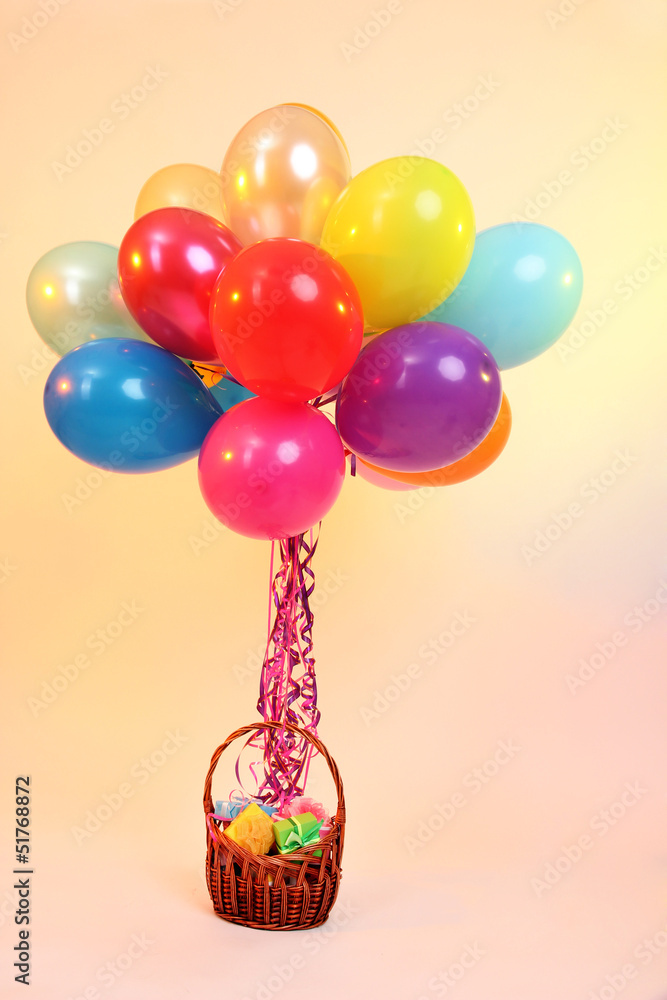 Many bright balloons and basket with gifts on orange background