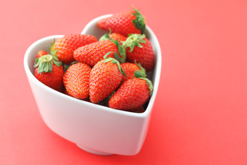 Wall Mural - Strawberry in heart shape bowl on red background