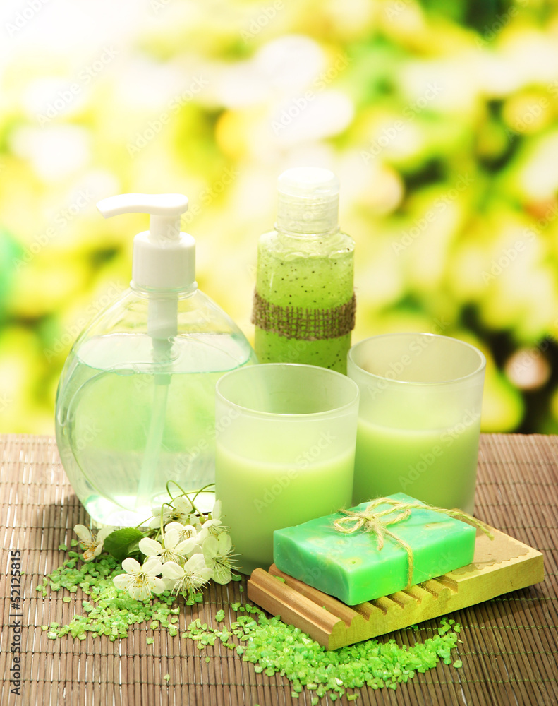 Cosmetics bottles and natural handmade soap on green background