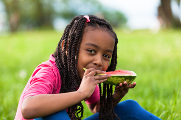 Outdoor portrait of a cute young black little girl eating waterm