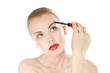 Beautiful woman applying cosmetics mascara brush on white.