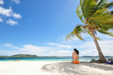 Young Bikini Girl Sits In Coconut Tree Shadow On White Beach
