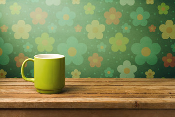 Green mug on wooden table over floral wallpaper