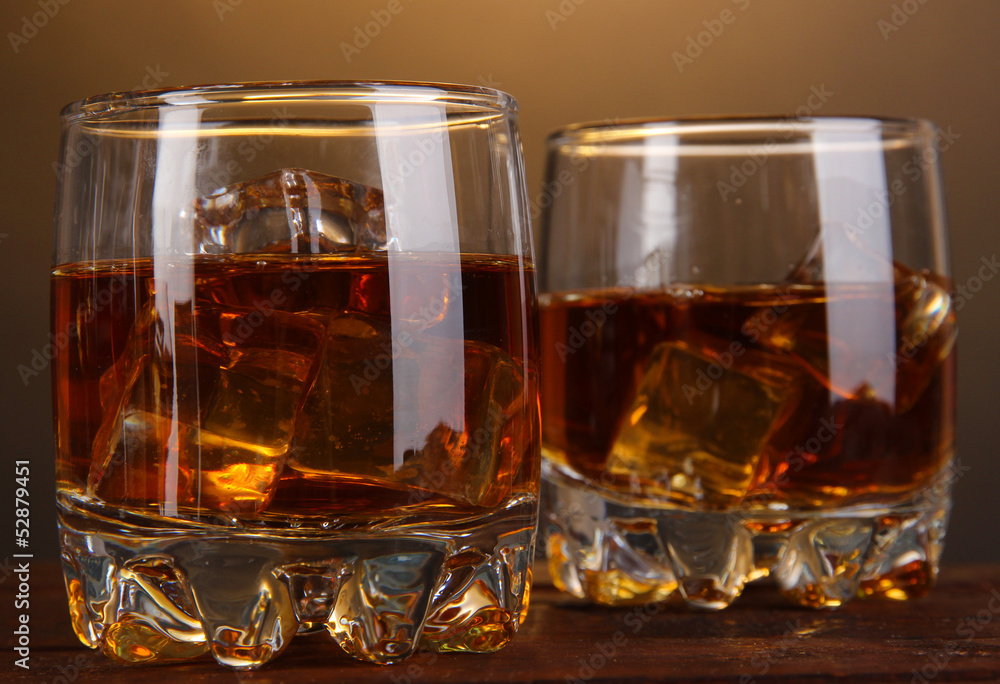 Brandy glasses with ice on wooden table on brown background