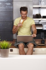 Poster - Young man using laptop on kitchen counter