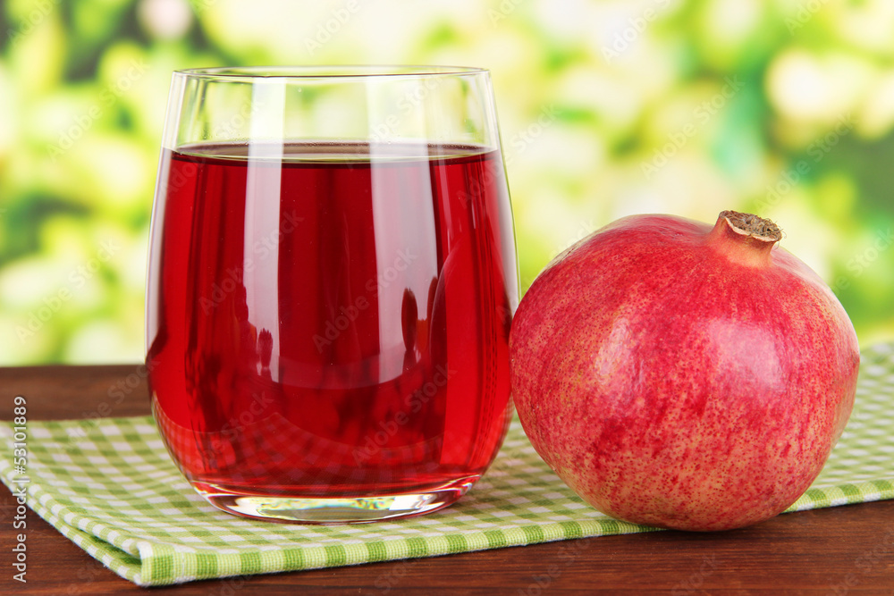 Glass of fresh garnet juice on table on bright background