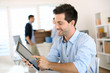© goodluz - Smiling man in office working on digital tablet