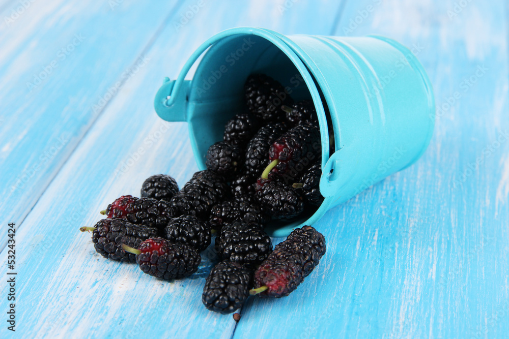 Ripe mulberries in bucket on wooden background