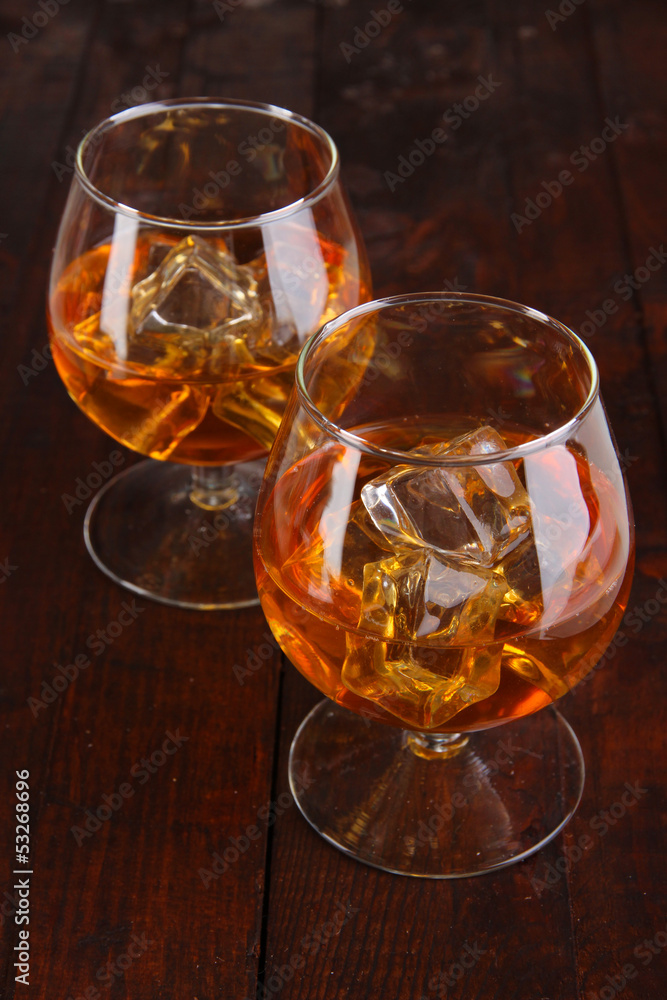 Brandy glasses with ice on wooden background