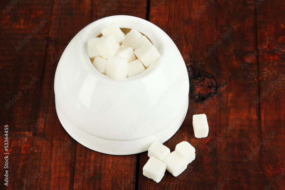 Refined sugar in white sugar bowl on wooden background