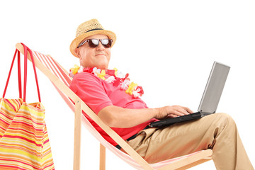 Wall Mural - Mature male tourist on a sun lounger with a laptop