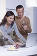© xixinxing - Mature Couple Looking at Laptop in the Kitchen, Drinking Wine
