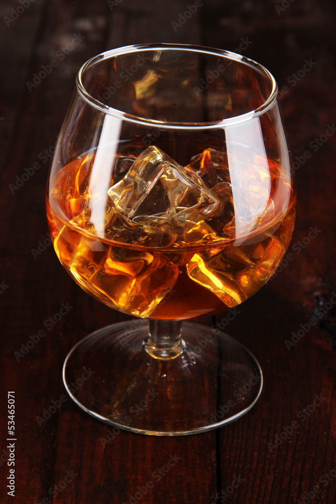 Brandy glass with ice on wooden background