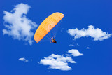 paraglider flying in a blue sunny sky with clouds