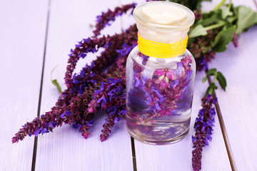 Poster - Medicine bottle with salvia flowers on purple wooden background