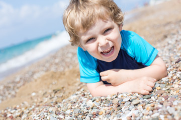 Wall Mural - Little toddler boy playing with sand and stones on the beach