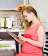 © Ermolaev Alexandr - pregnant woman using a tablet computer in kitchen