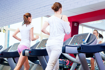 Two young sporty women run on machine