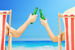 Man and woman relaxing on a beach and cheering with beer