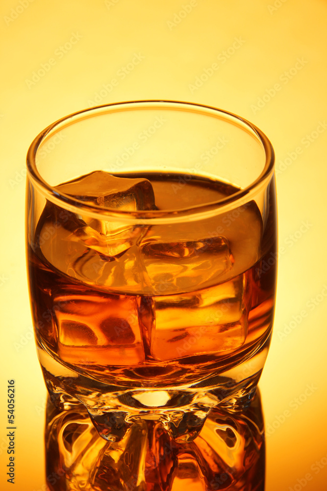Brandy glass with ice on yellow background