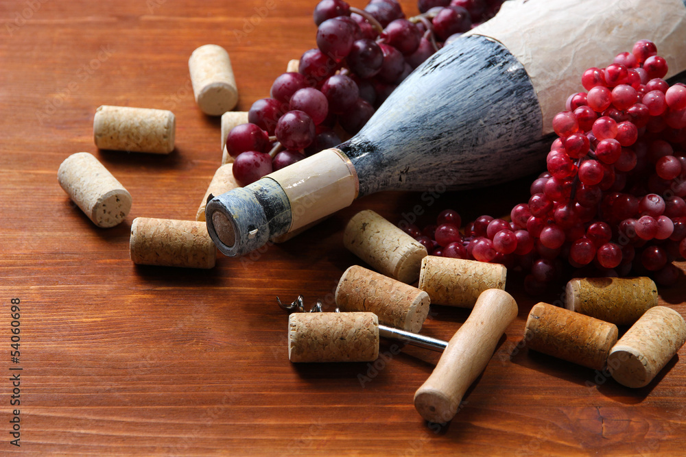Old bottle of wine, grapes and corks on wooden background