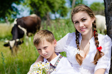 Teenage Sister And Little Brother Sitting By Cow Herd