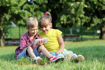 Wall Mural - boy and little girl play with tablet pc in park