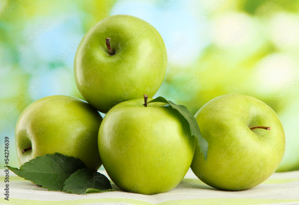Ripe green apples with leaves, on table, on green background