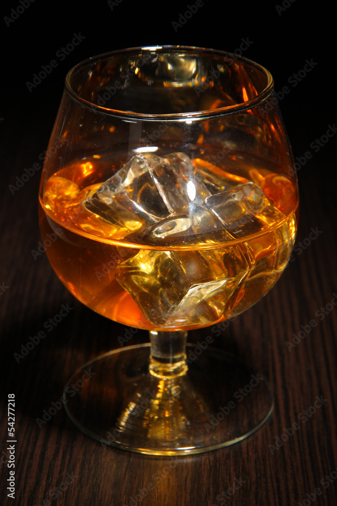 Brandy glass with ice on wooden background