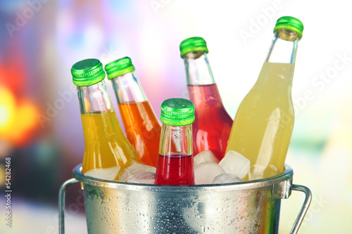 Obraz w ramie Bottles with tasty drinks in bucket with ice cubes, in bright